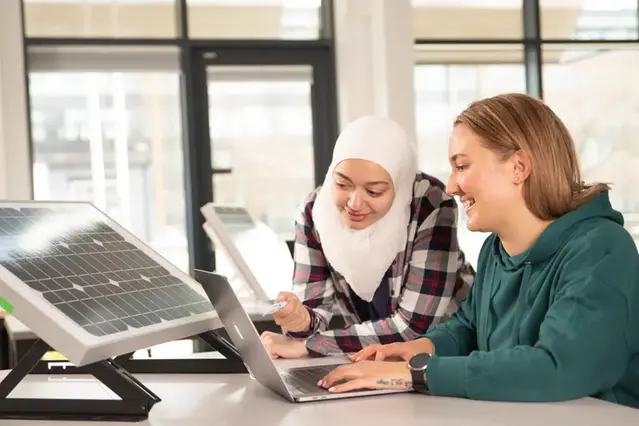 Två studenter arbetar via en laptop bredvid en solcellsprototyp.