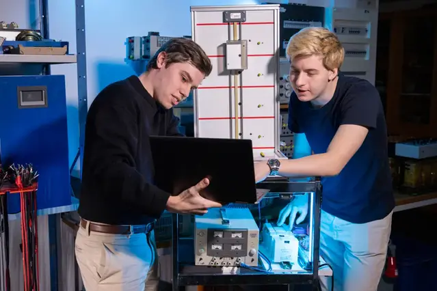 Två studenter står i en labbiljö och diskuterar vid en laptop.