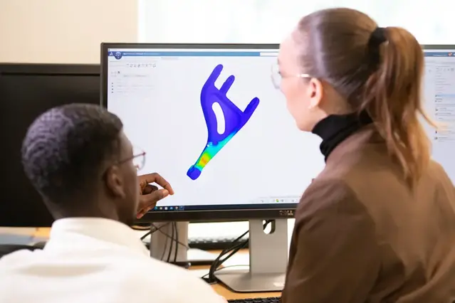 Två studenter tittar på en CAD-skiss på en datorskärm.