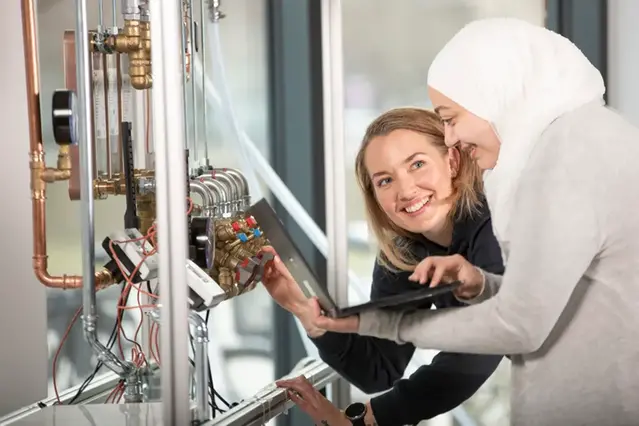Två kvinnliga studenter undersöker en pump i en labbmiljö.