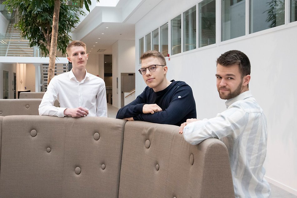 Tre personer som står lutade mot en soffa.