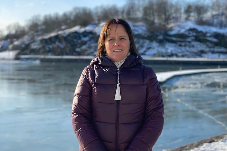A woman standing in a thick winter jacket in front of a frozen lake. Photo.