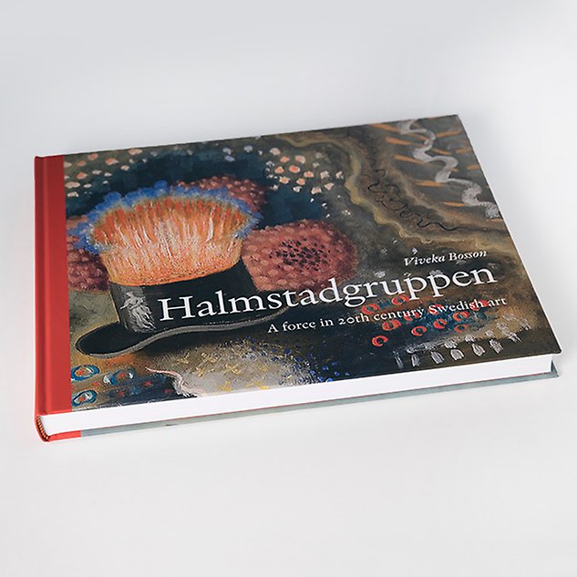 En bok med en målning i dunkla färger som omslag och texten ”Halmstadgruppen” ligger på en vit bakgrund. Foto.