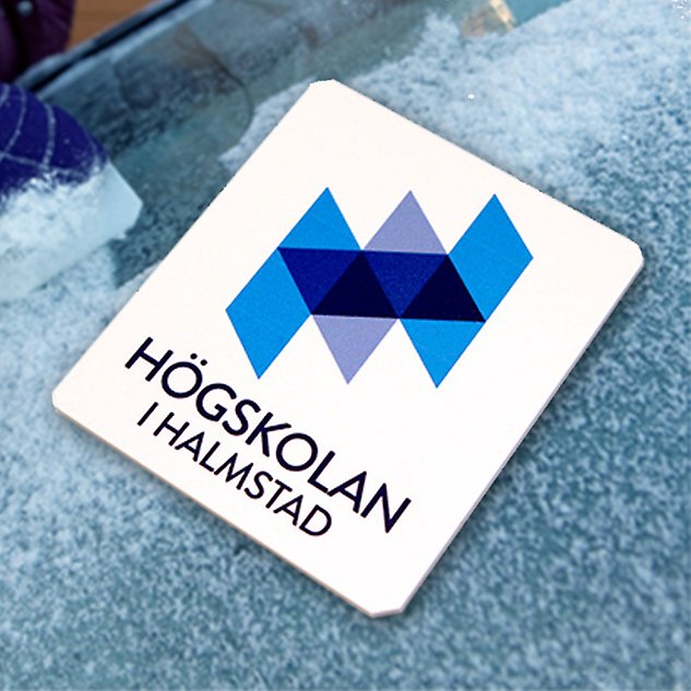 En vit isskrapa med Högskolan i Halmstads logotyp ligger på en bakgrund av is. Foto. 