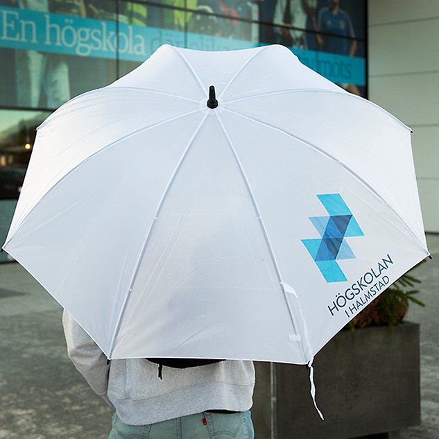 En person, sedd bakifrån, står under ett vitt, utfällt paraply. Foto.