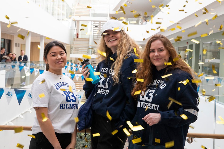 Three women dressed in merchandise behind falling confetti. Photo.