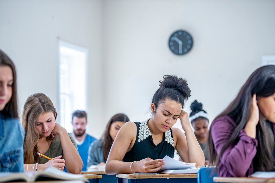 A classroom full of people focused on a sheet of paper in front of them. Photo.