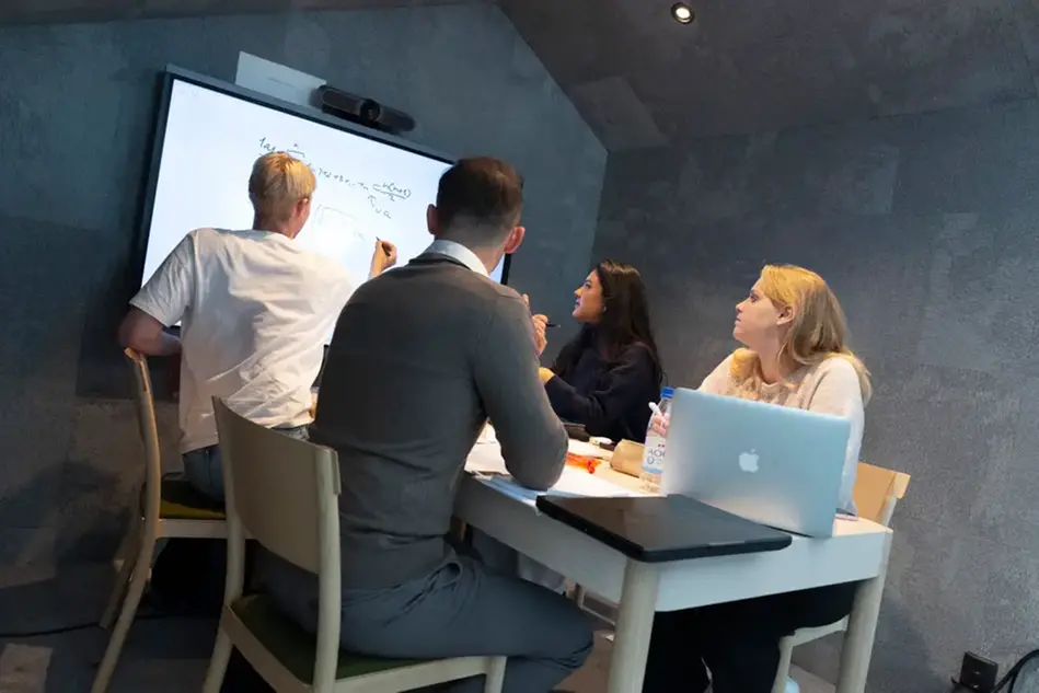 Tre personer ser in i kameran och ler. De lutar sig mot ett glasräcke i en ljus lokal. Foto.