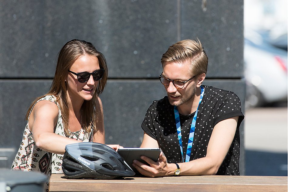 A female and a male student sitting outside looking at a laptop. Photo.