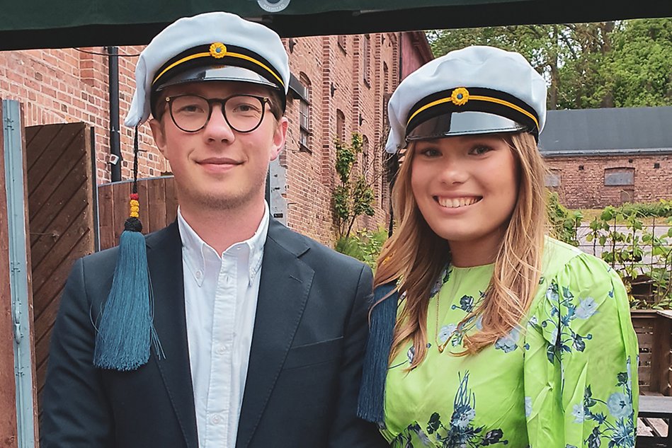 Glada och nöjda studenterna Nils Salonen och Ellen Brenander i finkläder och studentmössor.