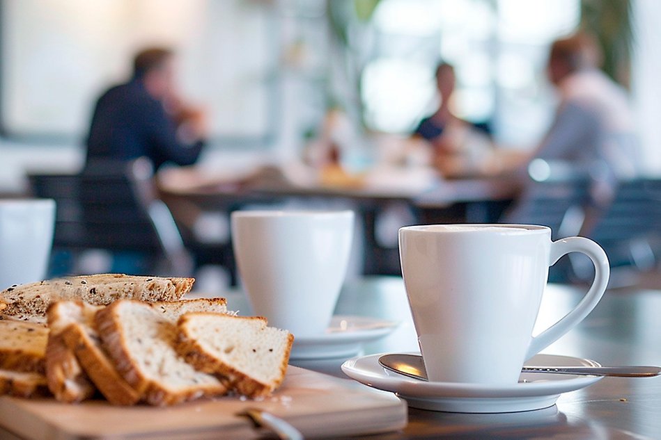 sliced bread, two white cups and people talking in the background. Photo.