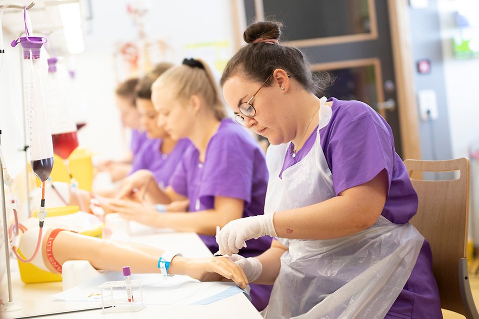Sjuksköterskestudenter sitter och tar blodprov i låtsasarmar
