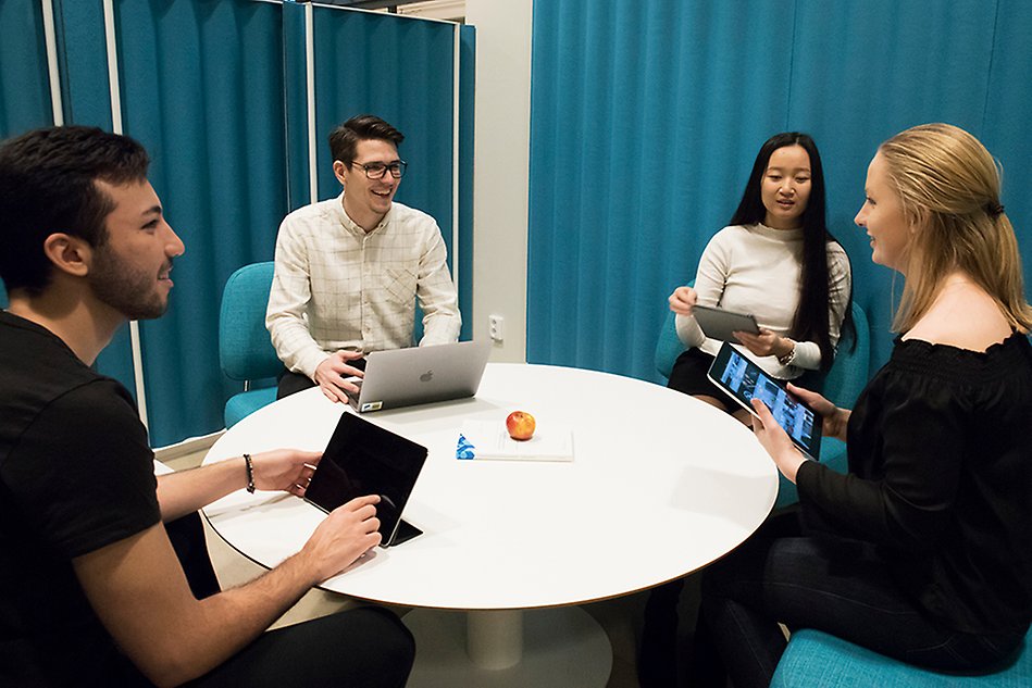 Four people sitting at a round table and talking, they all have laptops or tablets. Photo. 