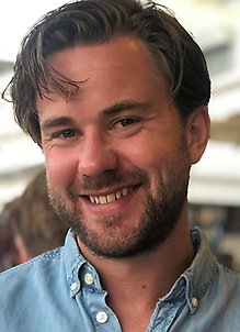 Person med kort hår ler in i kameran. Porträttfoto.