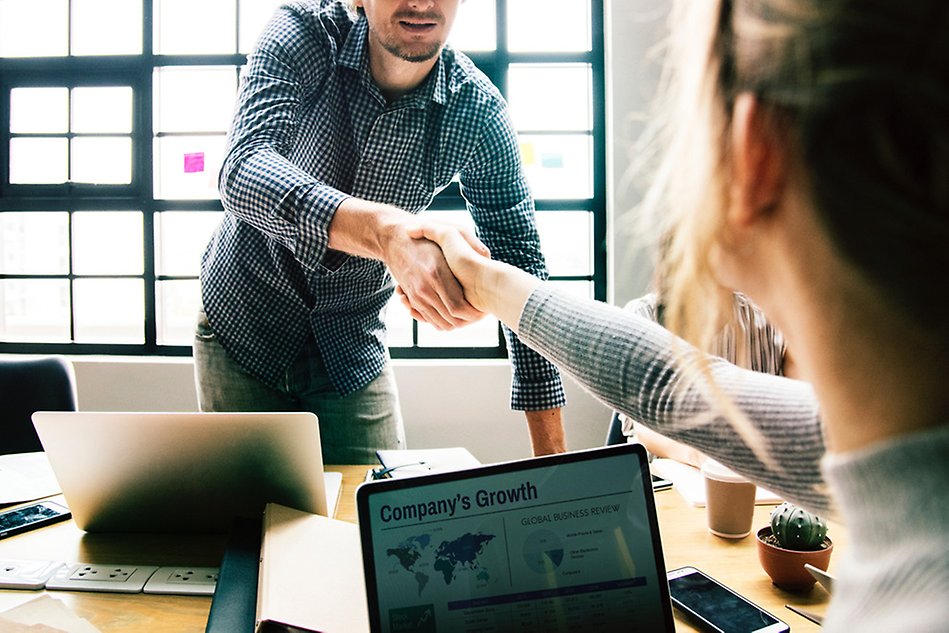 A man leaning over a table shaking the hand of a woman sitting across from him. Photo.