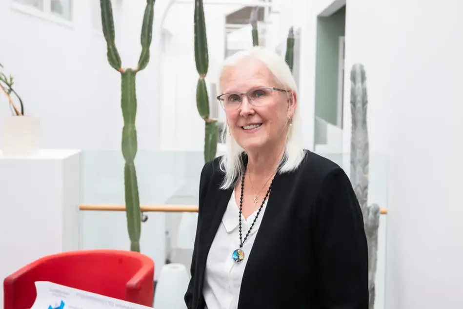 En person med långt ljust hår och glasögon ler in i kameran. Foto