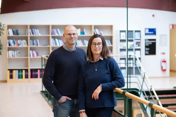 Man och kvinna i mörka kläder står framför en bokhylla. 