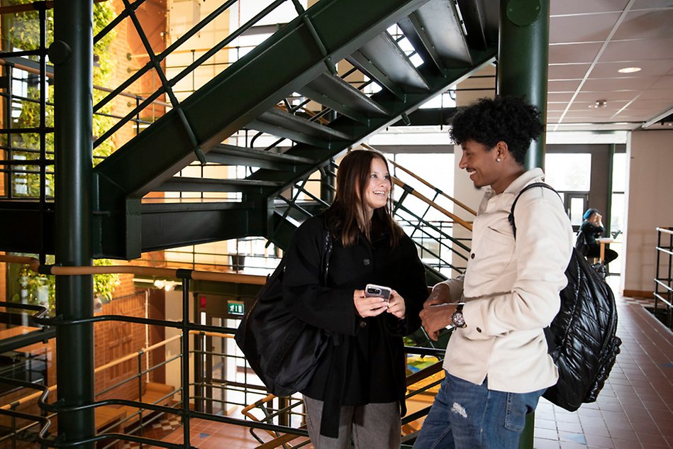 Two people talking with smiles on their faces, with a green staircase in the background.