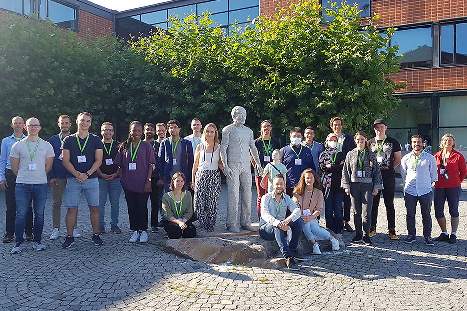 A group of people standing outdoors around a statue. Photo.