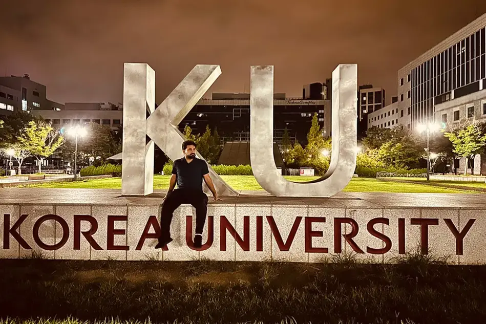 En man i svarta kläder sitter på en platå där det står Korea University.