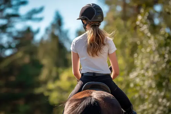 Ung person som rider på en häst, sett bakifrån.