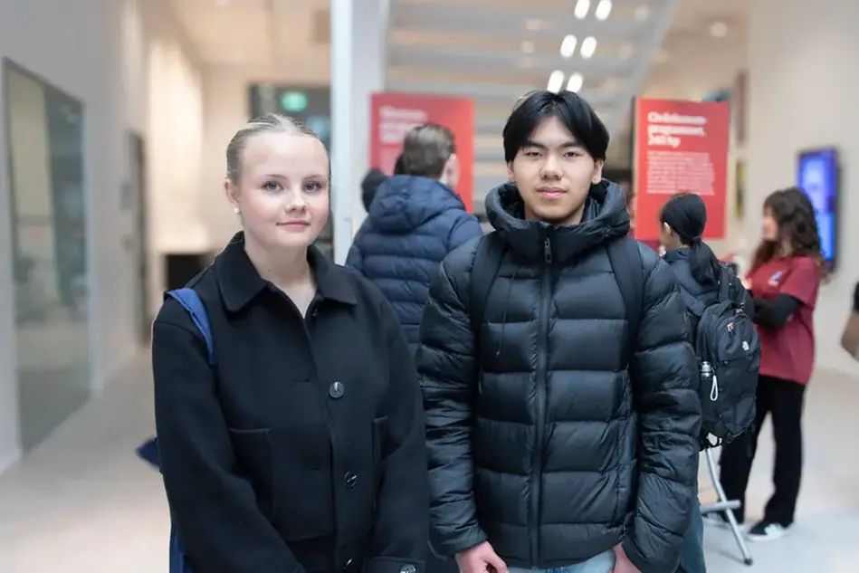 Två unga personer, en med ljust hår och en med mörkt hår, står bredvid varandra.