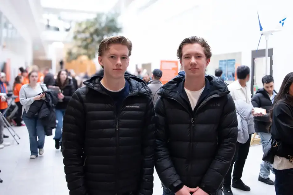 Två unga personer med ljust hår och svarta jackor står bredvid varandra och ser in i kameran.