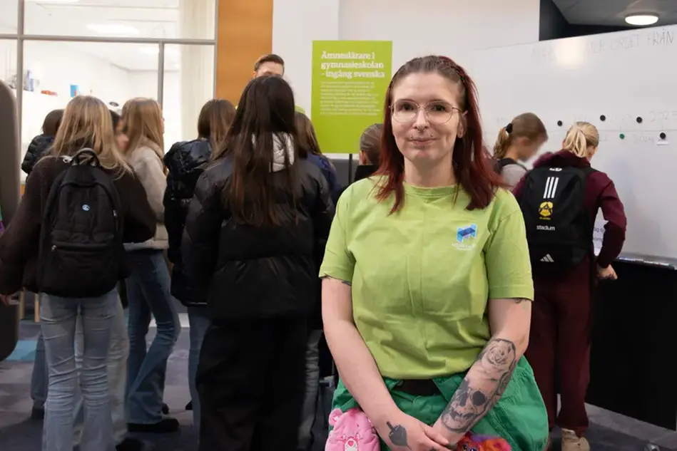 En ung person i grön t-shirt. I bakgrunden syns en grupp av minglande människor.