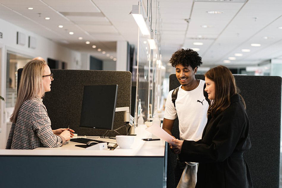 Two students are in the Service Center and a worker is talking to them. Photo.