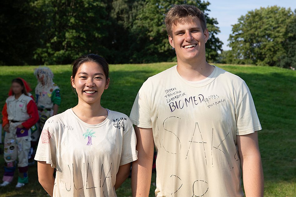 A young woman and a young man stand next to each other outdoors in a park. They look into the camera and smile. Photo.
