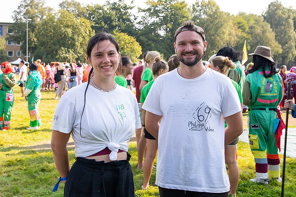 A young woman and a young man in white T-shirts smile and look into the camera. They are in an outdoor park. Photo.