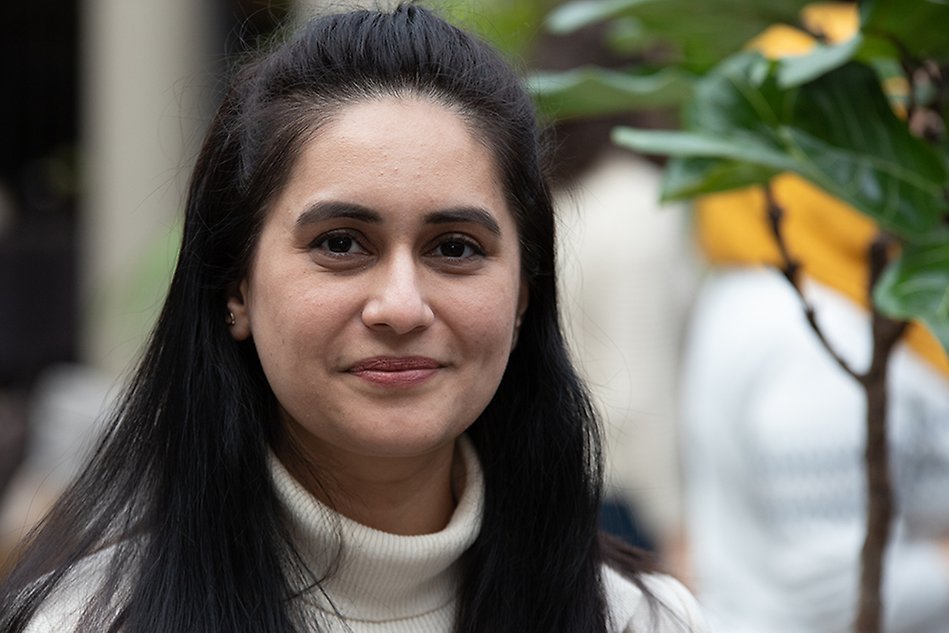 A woman stands infront of a plant and smiles into the camera.