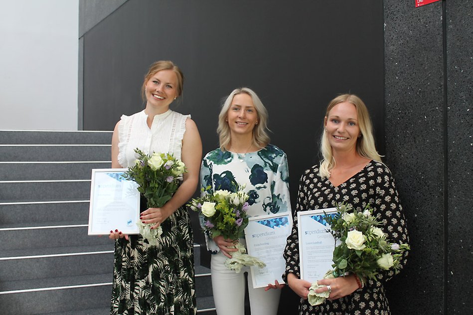 Tre studenter står med blommor och diplom.