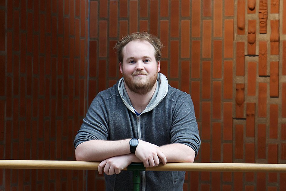 Man leaning on a rail, red brick wall in the background. Photo.