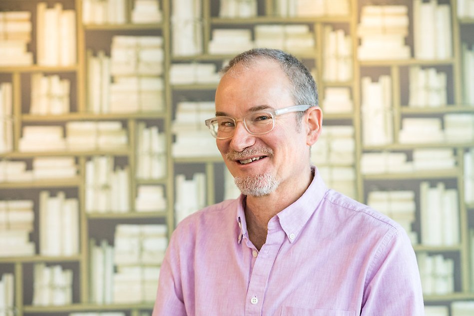 Man standing in front of a wall smiling and looking in the camera.