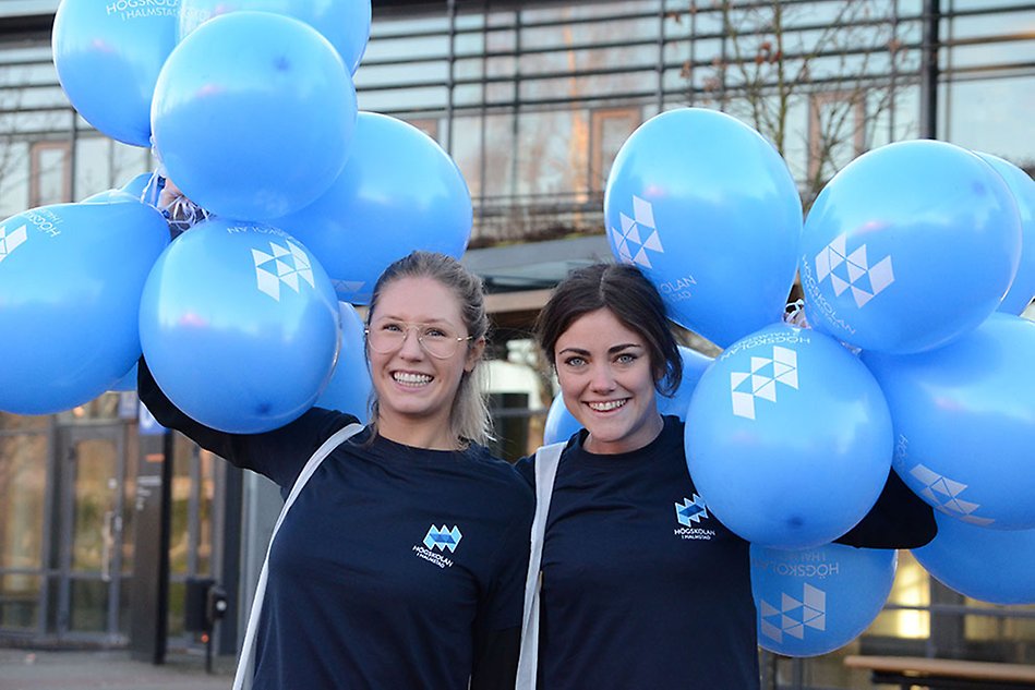 Two girls holding blue balloons smiling at the camera. Photo.