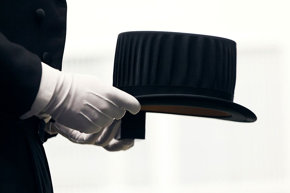 Two hands clad in white gloves holding a black top hat. Photo.