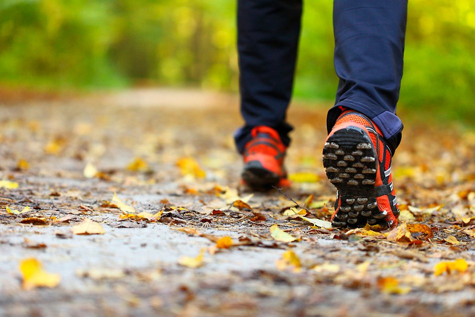 Two feet walking on a path covered in dry autumn leaves