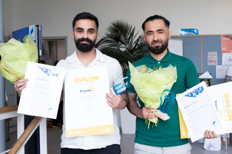 Two young men stand up and look into the camera. In their hands they have diplomas and flowers. Photo.