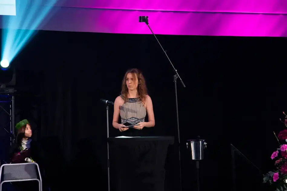 A woman in a festive dress stands on a stage and gives a speech.