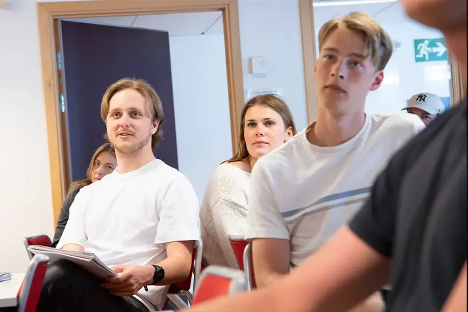Några unga personer sitter och ser ut att lyssna till någon som pratar. Foto