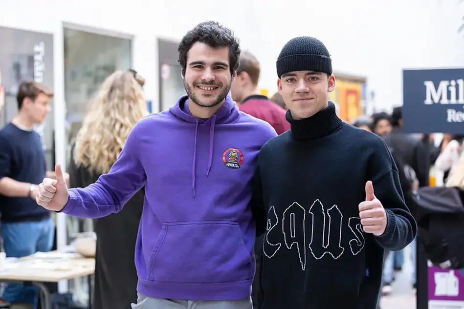 Två studenter gör tummen upp mot kameran och ler. Foto.