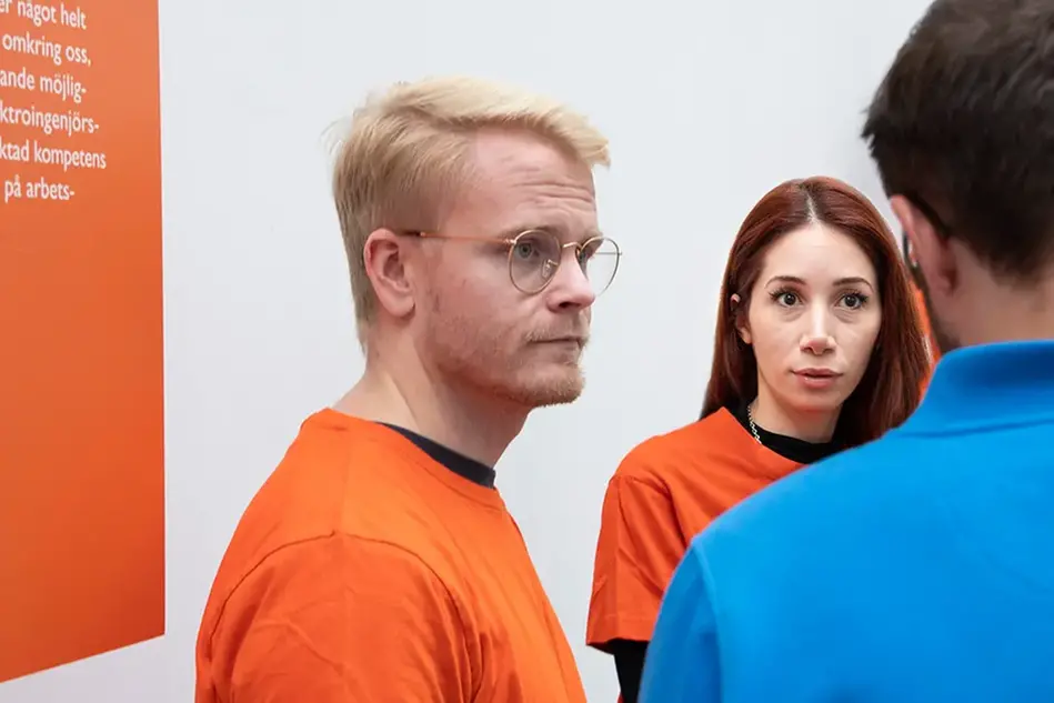Un man och en kvinna står bredvid varandra och ser på en man som intervjuar dem.