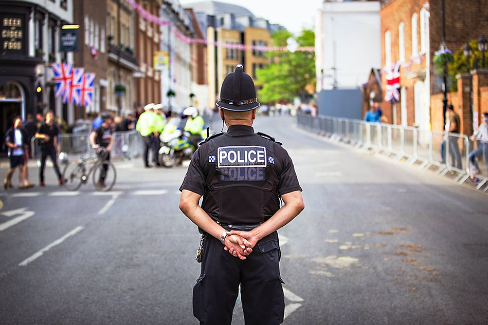 A police officer standing in the street, hands clasped behind his back. Photo.