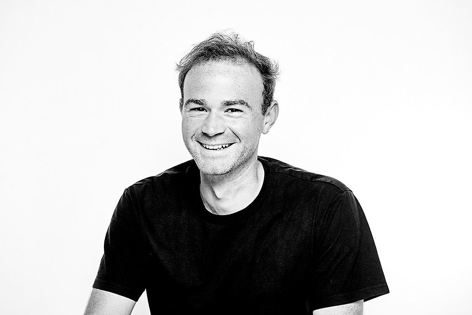 Black and white portrait of a smiling man with stubble, wearing a black t shirt. Photo.