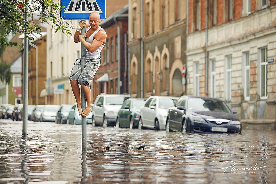 En man klamrar sig fast vid en stolpe för vägmärken, gatan nedanför är översvämmad. Foto.