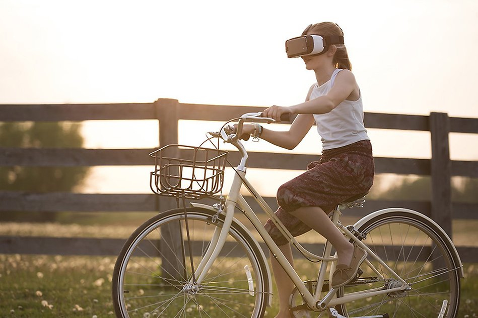 Flicka som cyklar i naturen, staket i bakgrunden, och på sig har hon VR-glasögon