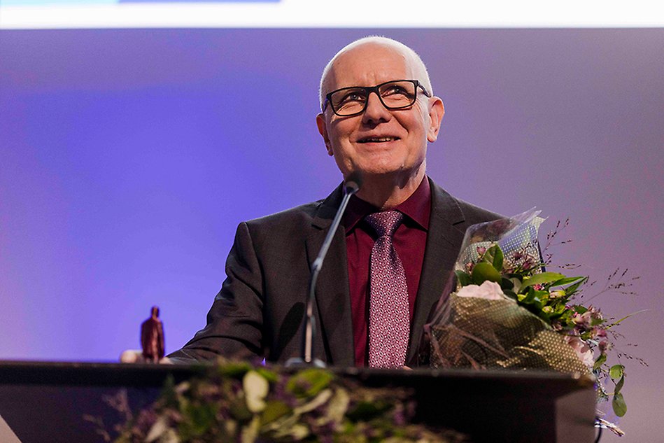 Man standing at a podium speaking, dressed in a suit. Photo.