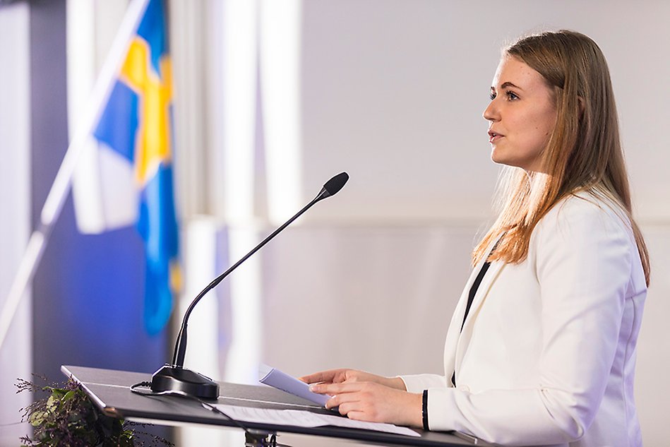 Woman in white suit jacket holding a speech