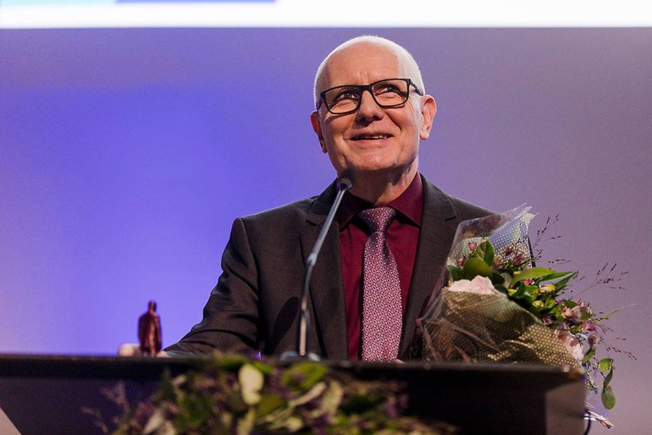 Man står vid talarstol med en bukett blommor